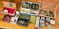 Overall view of multiple boxes full of assorted costume jewellery and accessories on a wooden surface.