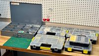 Wide view of six plastic fastener storage boxes on a workbench, showing variety of compartmentalized fasteners inside.