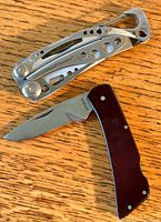 Photo showing Gerber folding knife with black handle and Leatherman Skeletool multi-tool on wood surface.