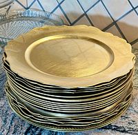 Stack of gold-tone chargers with scalloped edges showing size and condition.