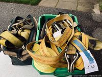 Green containers filled with multiple yellow heavy duty ratchet straps with attached metal hooks and ratchet tensioners.