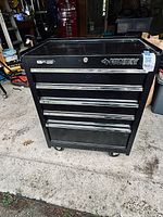 Front view of closed black Husky tool chest on caster wheels, showing five drawers and brand logos.