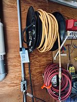 Yellow industrial air hose coiled on Rapid Reel hose reel mounted on the wall near other tools and equipment.