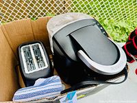 Box containing black Keurig coffee maker with water reservoir, black 2-slice toaster, and a cloth.