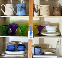 Full view of kitchen cabinet contents showing stoneware pitchers, glass dessert cups, Corelle plates, and condiment dishes.