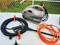 Kodiak D-11 power washer with two wands and cables placed on a white table outdoors, near a fence.