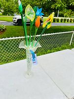 Full view of the clear glass vase holding six colorful handblown glass flowers outdoors, showing size and shape