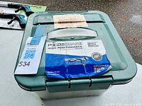 Closed large plastic container with green lid showing Pozisquare label identifying outdoor screws inside