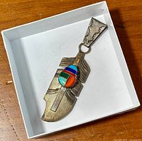 Top-down photo showing the size and design of the silver feather-shaped pendant with colorful inlaid stone.