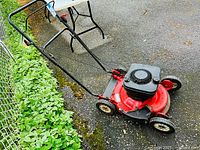Full view of red gasoline lawn mower showing black handlebar and four wheels.