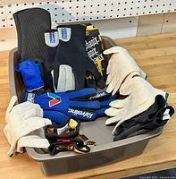 Top view of the assortment of gloves in a beige plastic bin on a wooden workbench against a pegboard background. The collection includes various gloves from Mechanix, Valvoline and cotton gloves in multiple colors and styles.