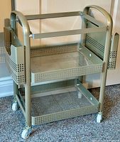 Full view of the grey metal mobile organizing cart showing top open frame and two mesh trays with side slots and wheels.