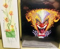 Two artworks together: one is a framed floral original painting with orange and green tones; the other is a framed signed print of a clown face with fiery hair and sharp teeth on dark background.
