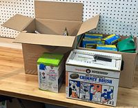 Overview of the lot showing the chimney brush kit box, Dust Off 4-pack box, lint traps, and blue gloves on a workbench.