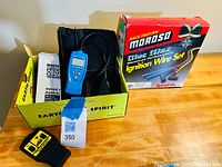 Photo showing the digital OBD2 car reader inside a yellow Earth Spirit box alongside the Moroso ignition wire set box on a wooden surface.