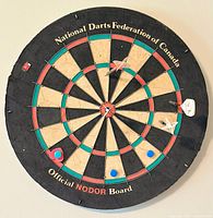 Front view of official size dart board labeled National Darts Federation of Canada and Official NODOR Board with darts and mounting pins attached.