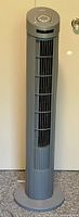 Full view of the tall gray tower fan showing vertical front grille vents and round base.