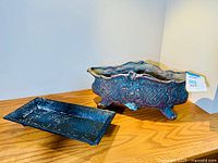 Front view of the painted cast metal planter and the metal tray placed beside it on a wooden surface