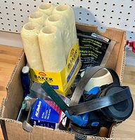 Wide view of the box containing all painting supplies including roller covers, respirator mask, rubber weather stripping, and small tools.