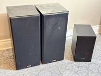 Two Paradigm 5se MK2 speakers on the left and a smaller Samsung PS-WT55D subwoofer on the right, all with black cloth grilles.