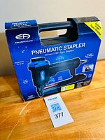 Photo of the pneumatic stapler in its original blue and black carrying case and box, showing product branding and features.