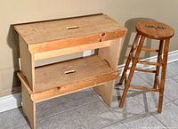 Pair of primitive wood benches and one wooden bar stool beside them on a tiled floor next to a beige wall.