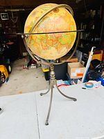 Full view of the globe on metal tripod stand on white table, garage background.