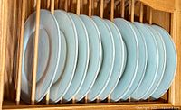 Eleven ceramic dinner plates stacked vertically in a wooden rack, showing the full set.