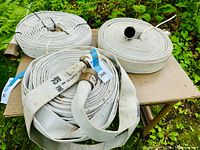 Three coiled white woven fire hoses placed on a small table outdoors, showing their size and condition.