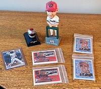 Lot of sports-related items including a Kirk Gibson baseball figurine standing on a small green base, a small replica race car helmet labeled 'Richard Ascroft 1998', and five sports trading cards.