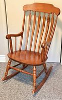 Full front view of the solid walnut rocking chair showing the complete design including curved backrest, vertical slats, armrest, contoured seat, and turned legs with rockers.