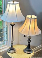 Two table lamps and the folding end table arranged together on carpet near window and wall