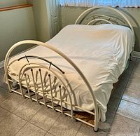 Full view of the queen sized metal bed frame with headboard and footboard showing white paint and bronze accent rods.
