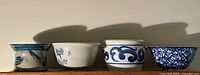 Four varying vintage blue and white pottery pieces in a row on a shelf showing different shapes and patterns
