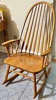 Full view of the oak rocking chair showing Windsor style back, armrests, contoured seat, and curved rocker legs.