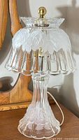 Full front view of the crystal glass boudoir lamp showing scalloped shade with etched leaf design and brass finial on top.