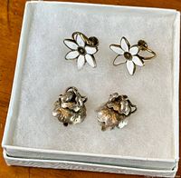 Top-down photo showing both pairs of earrings in a white box; white enamel daisy earrings at top, silver acorn and oak leaf earrings at bottom.