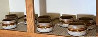 Eight vintage Laurentian pottery soup cups lined up on a shelf. Cups have a brown and textured white lower glaze with single handles visible from the side.