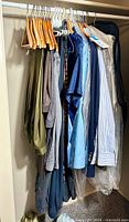Photo showing men's formal wear hanging in closet including jackets, suits, and shirts mostly in blues and neutral colors