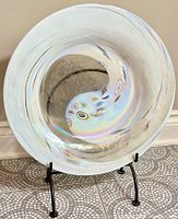 Front view of circular opalescent glass plate with iridescent finish and colorful patterns on a black metal stand