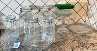 Overview of all vintage pressed glass items and sealer jars on countertop showing various shapes and sizes.