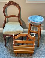 Photo of antique carved wooden chair, primitive pine magazine rack, and cushioned vintage stool in room setting