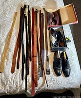 Photo showing multiple belts and two pairs of men's shoes on a white quilted surface, one shoe pair in an open box