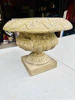 Side view of vintage cast planter urn showing detailed rim and textured body on square base.