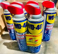 Front view of six new unopened WD-40 cans with red spray nozzles showing the smart straw design.