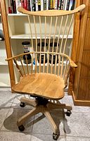 Front view of the wooden Windsor back chair with armrests and contoured seat, showing wheels and swivel base.