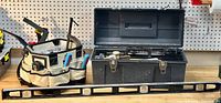 View of carpenter's tool bag full of hand tools, black metal toolbox with lid open showing tools inside, and large metal level in front