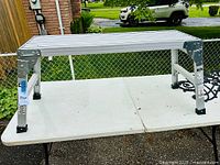 Front angle view of aluminum work platform showing silver slatted top and metal corner braces.