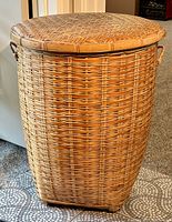 Tall woven wicker laundry hamper positioned on tiled floor, showing full height and shape.