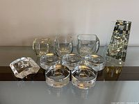 Photo showing all 10 clear glass pieces arranged on a surface including round tealight holders, small rounded bowls, a square candle holder, and a tall prism piece.